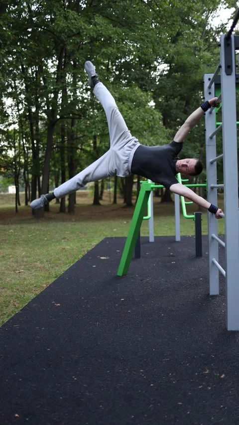 Vertical screen young man performs human flag exercise on outdoor bar holding bo Stock Footage 316700365