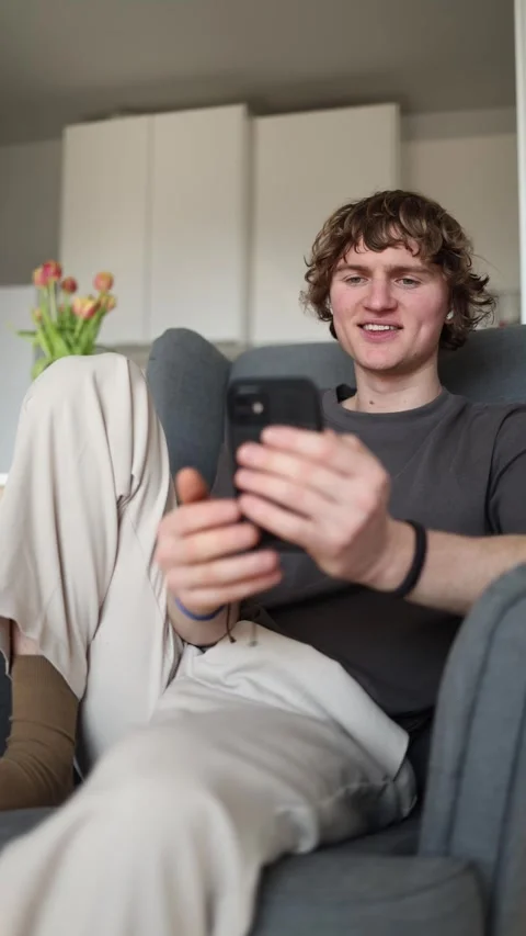 Vertical screen: Young man sending an air kiss through his smartphone while rela Stock Footage 302632452