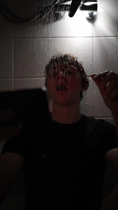 Vertical screen young man sits under shower streams stretching arm forward with  Stock Footage 316066172