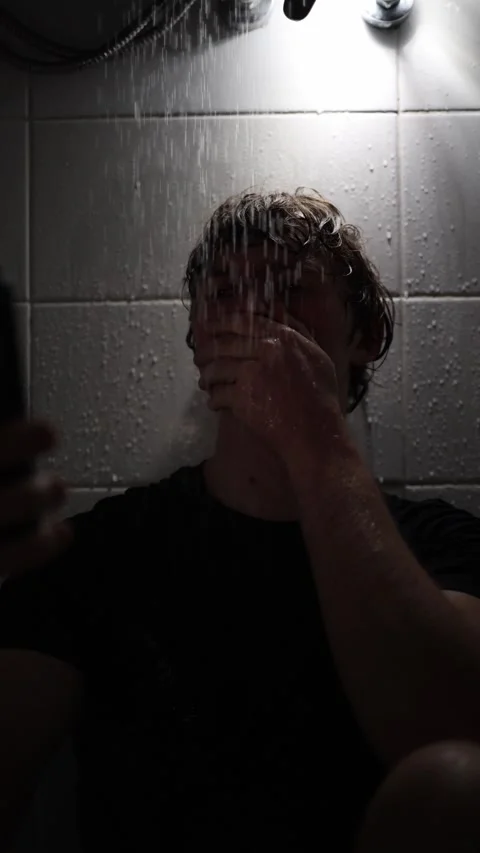 Vertical screen young man sits under shower holding smartphone covering mouth wi Vídeo Stock 316066190