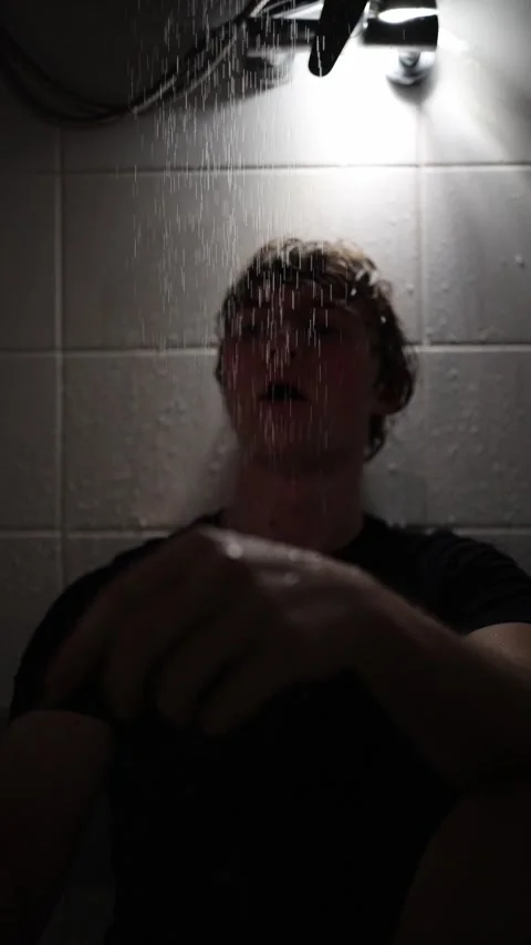 Vertical screen young man sits under shower holding smartphone at arm’s length w Stock Footage 316066197