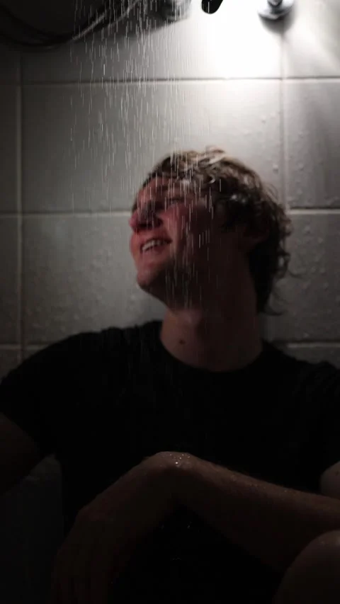 Vertical screen young man sits under shower streams in dim light head tilted bac Stock Footage 316066205