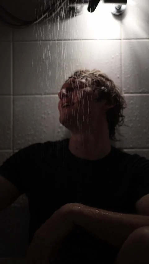 Vertical screen young man sits under shower holding smartphone water pouring dow Stock Footage 316066221
