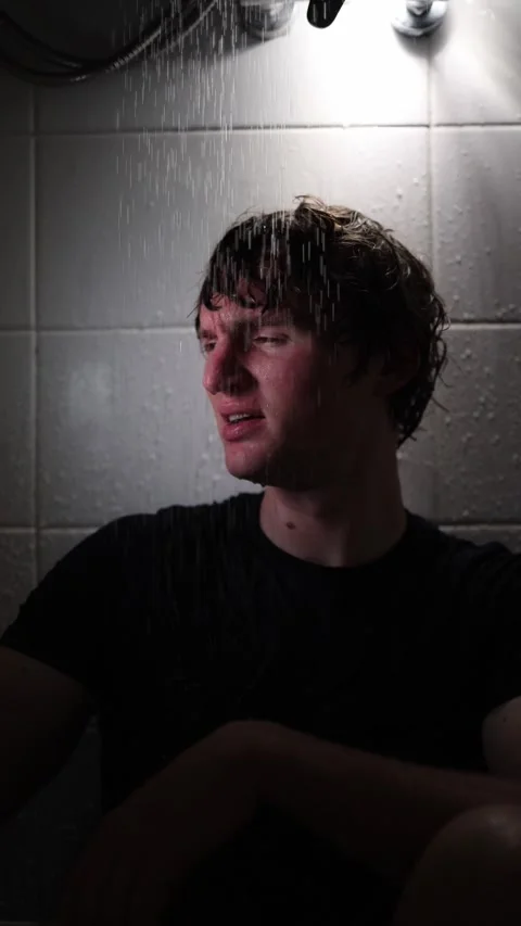 Vertical screen young man sits under shower holding smartphone as glow lights hi Stock Footage 316066243