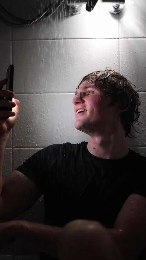 Vertical screen young man sits under shower holding smartphone scrolling through Stock Footage 316066295