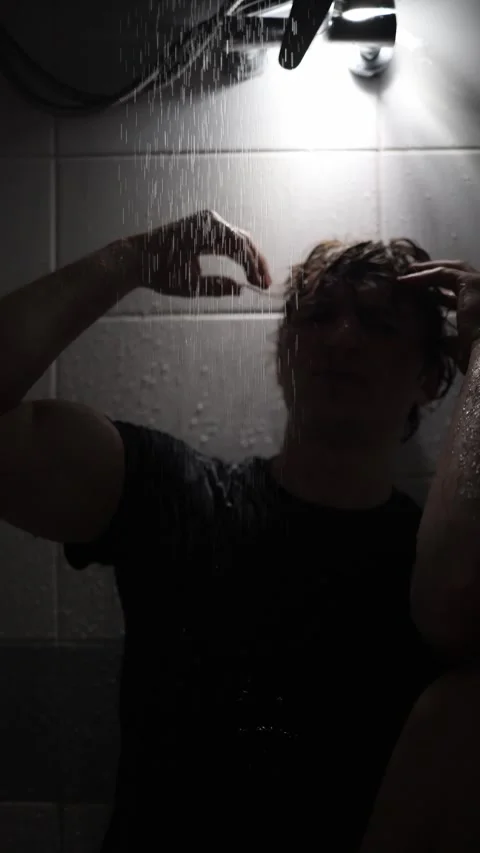 Vertical screen young man sits under running shower pressing hands to wet hair w Stock Footage 316066309