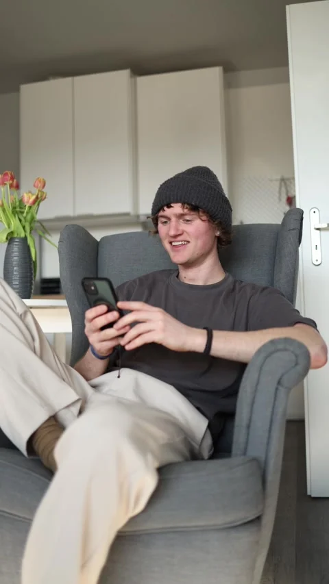 Vertical screen: A young man is sitting in a chair, smiling while engaging in an Stock Footage 302633247