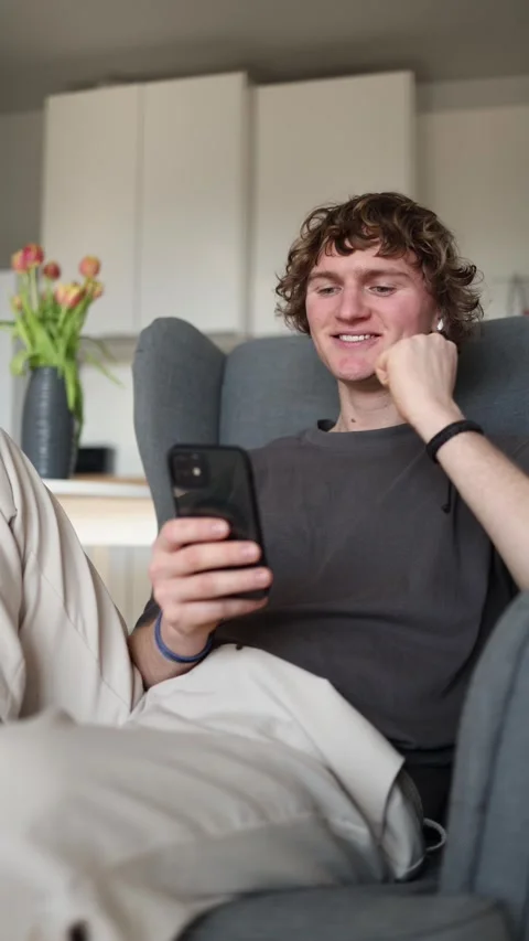 Vertical screen: Young man smiling joyfully at smartphone after receiving a posi Stock Footage 302632183