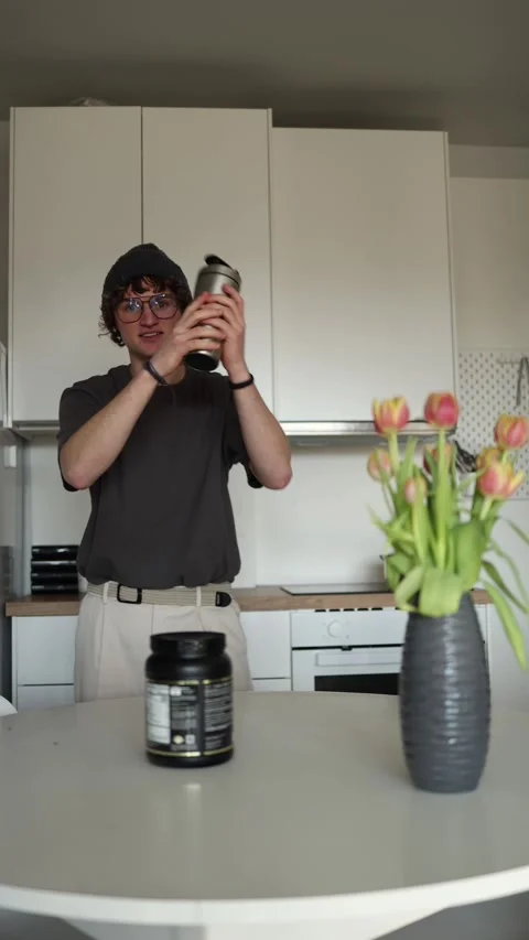 Vertical screen: The young man is smiling, holding a shaker in both hands as he  Stock Footage 302633483