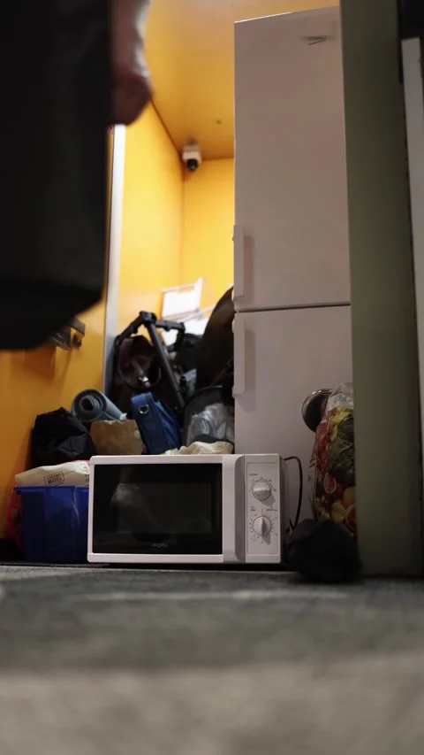 Vertical screen young man in socks bends over to lift storage box from cluttered Stock Footage 309330694