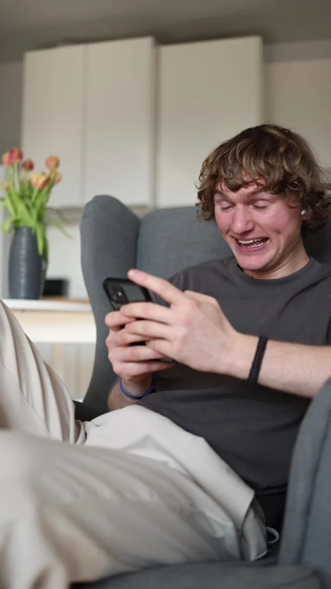 Vertical screen: Young man staring dumbfounded at his smartphone, visibly becomi Stock Footage 302632312