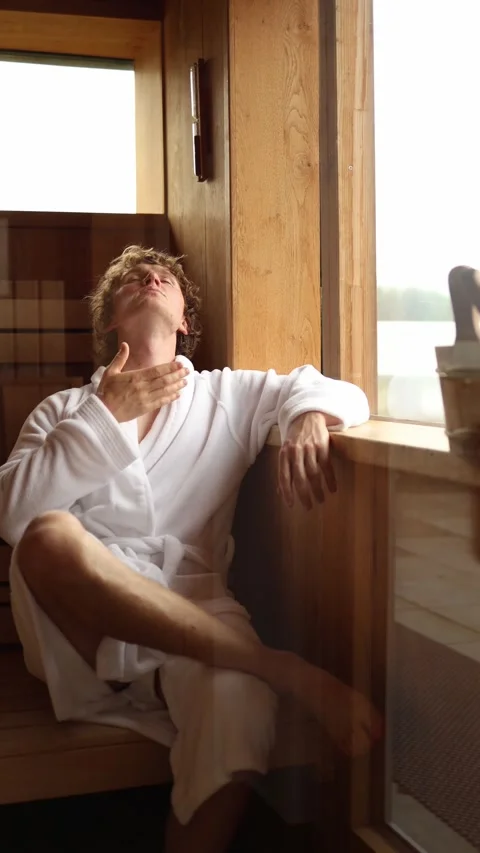 Vertical screen young man in white bathrobe enjoying sauna heat sitting by woode Stock Footage 318217459