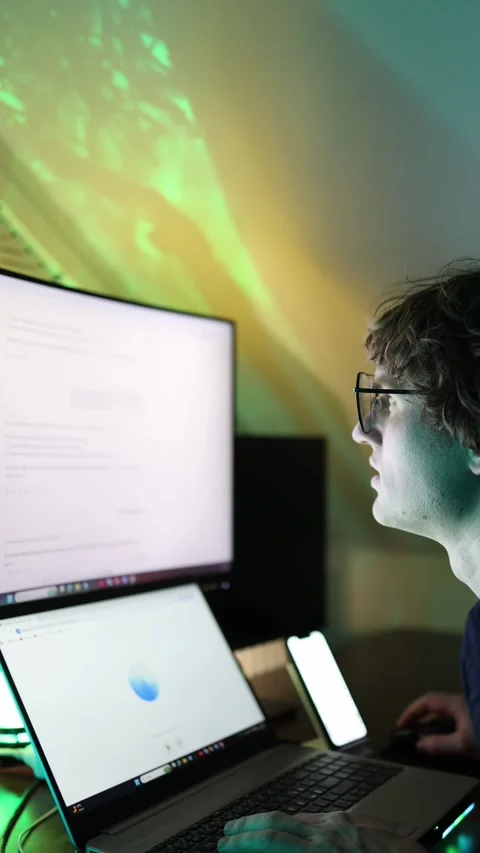 Vertical screen young man works late at computer with dual monitors using artifi Stock Footage 316878105