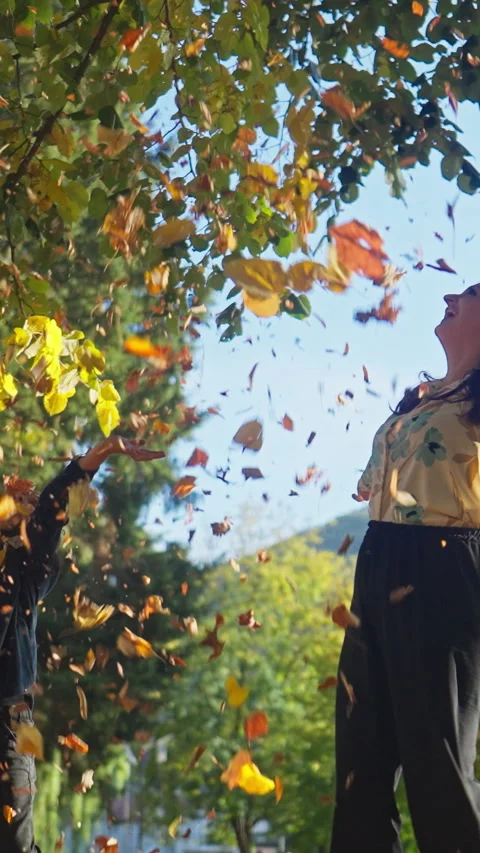 Vertical Screen: Young Mother Throwing Fallen Dry Autumn Leaves Up with Her Son Stock Footage 281158339