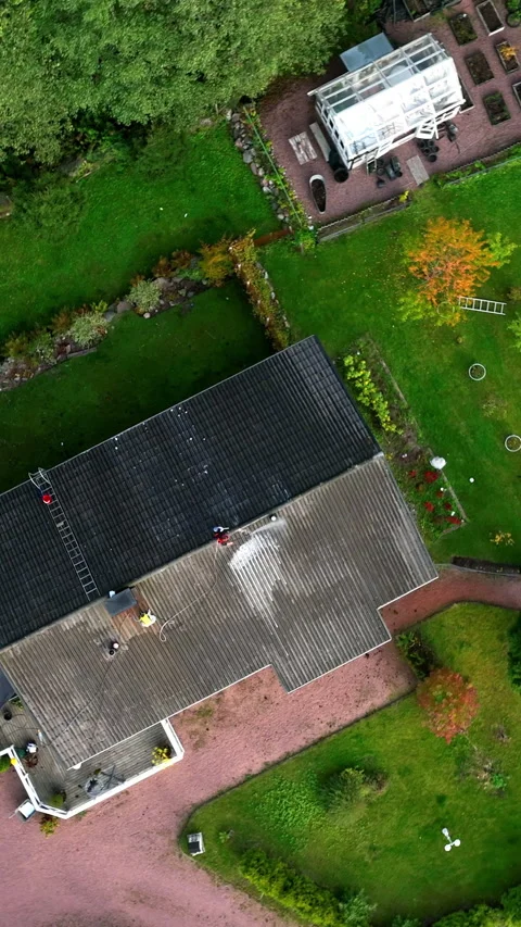 Vertical screwdriver drone shot above a woman washing a house roof to remove Vídeos de archivo 335908226
