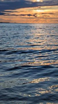 Vertical sea surface closeup with glowing sunset reflections and smooth water in Stock Photos