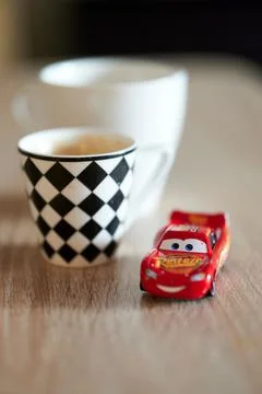 Vertical shallow focus of Lightning McQueen toy car next to cups of coffee on a Stock Photos