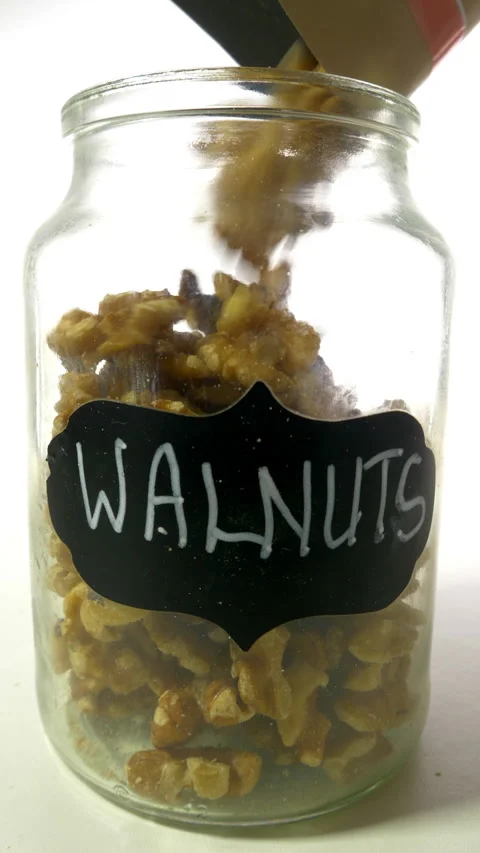 Vertical - Shelled walnuts pouring from a packet into a labelled glass jar. Stock Footage 282971334
