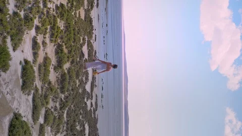 Vertical shoot of young female traveler walking by the beach towards sea in a Stock Footage