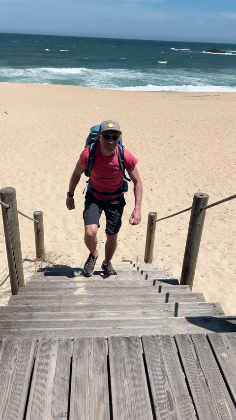 Vertical shot of active backpacker man walking by sandy beach and Atlantic Ocean Stock Footage 329791768