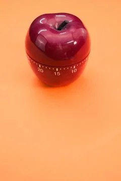 Vertical shot of an apple-shaped kitchen timer isolated on orange background Stock Photos