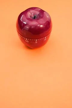 Vertical shot of an apple-shaped kitchen timer isolated on orange background Stock Photos