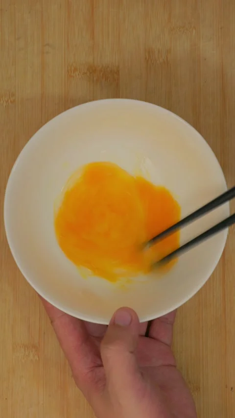 Vertical shot of asian hands whisking raw eggs quickly with wooden chopsticks. Stock-Footage 337449708