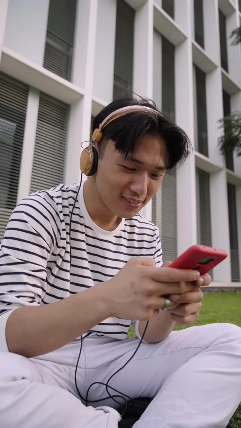 Vertical shot Asian student using smartphone chatting and laughing at campus Stock Footage 213677710