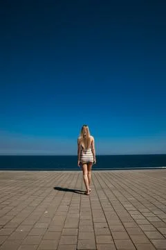 Vertical shot from back of long-haired young woman walking in sunny day. Fotos de archivo