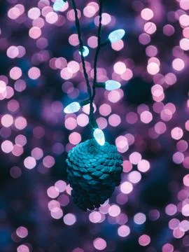 A vertical shot of a blue pine cone ornament hanging from string lights with  Stock Photos