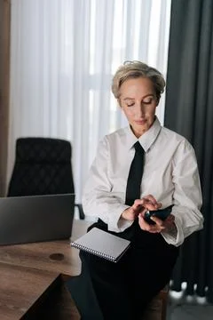 Vertical shot of busy middle-aged business woman using typing smartphone sitting Stock Photos