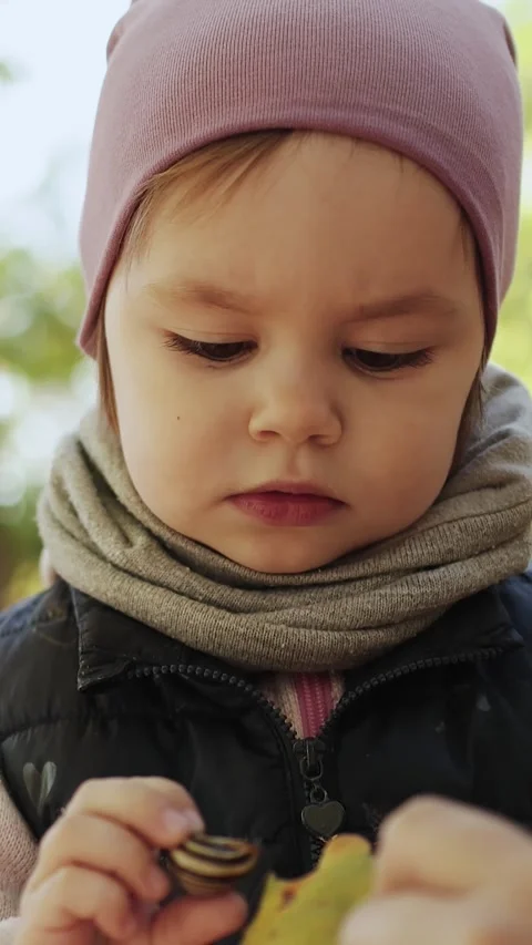 Vertical shot. A child in a pink hat is curiously looking at a snail shell she Stock Footage 308458145