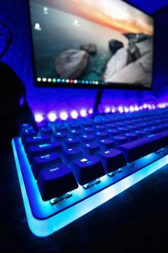 Vertical shot of a computer keyboard with neon blue light with a screen in the b Stock Photos