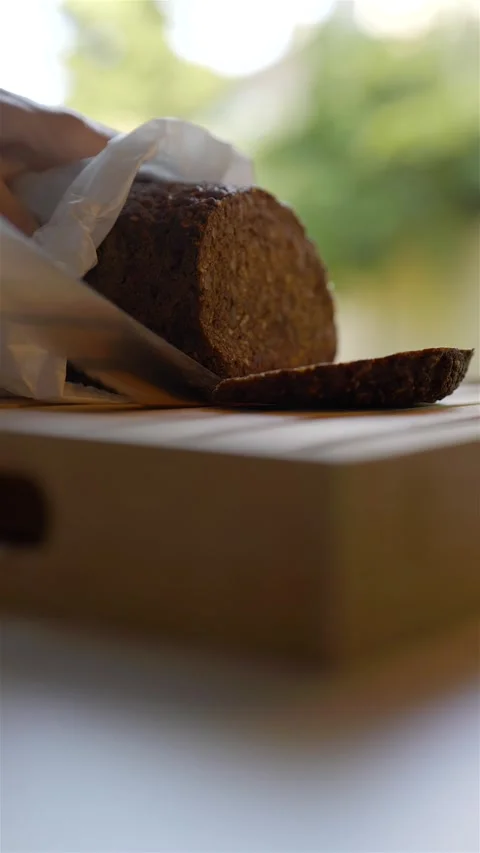 Vertical shot of cutting fresh dark baked bread with bread knife Видео 285319855