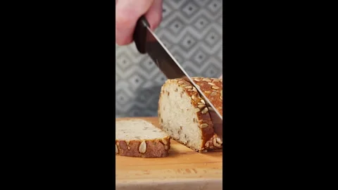Vertical shot. Dark bread is cut with a kitchen knife on a wooden board. Stock Footage 302633692