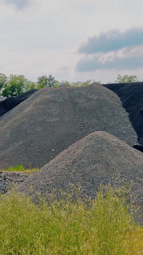 Vertical shot of dark crushed rock piles behind green grass field Stock Footage 343794414