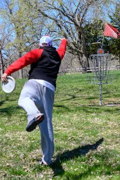 Vertical shot of a disc golf player throwing a disc in the park. Stock Photos