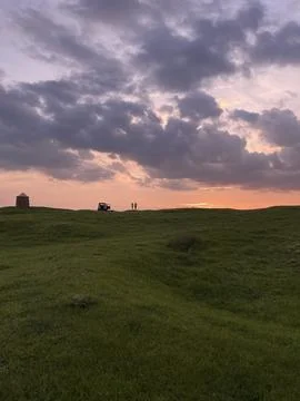 Vertical shot of dramatic cloudy sunset sky over green hill, couple watching  Stock Photos