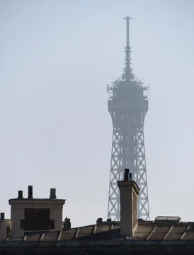 Vertical shot of the Eiffel Tower over the roofs of Paris shadowed by fog Fotos Stock