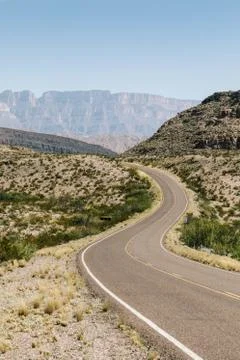 A vertical shot of an empty road in the middle of a dry field with bushes and Stock Photos