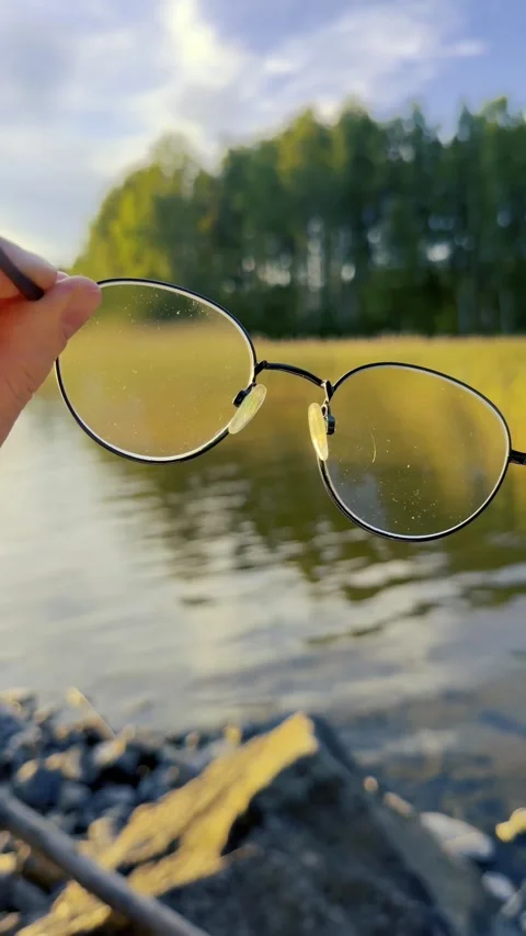 Vertical shot of eyeglasses held up at a lake at sunset Stock Footage 343126928