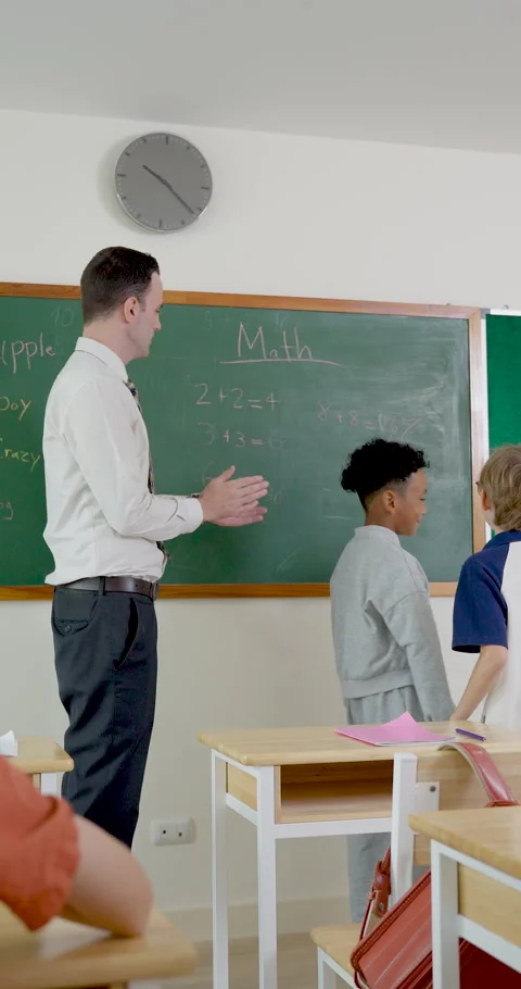 Vertical shot follows young boy pupil standing near chalkboard while male adult Video stock 336070193
