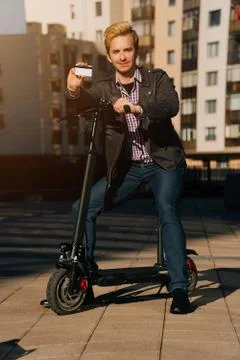 Vertical shot of a full-length man with an electronic scooter stands holding  Stock Photos