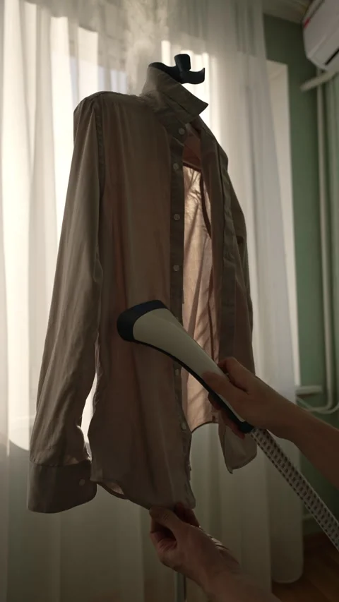 Vertical shot of homemaker steaming wrinkled beige shirt using handheld garment Stock Footage 305511580