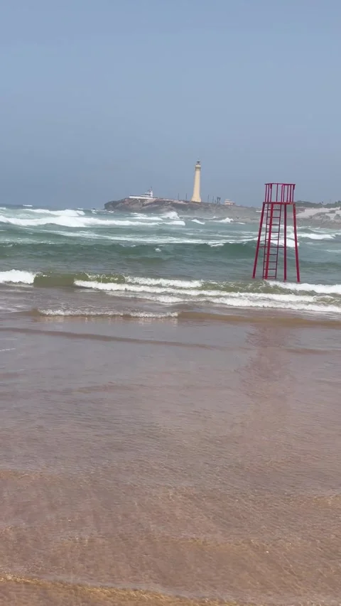 Vertical Shot of Lifeguard Tower and Distant Lighthouse on Ocean Beach Stock Footage 340775114