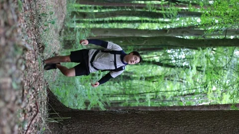 Vertical shot man climbing mountain in forest.guy walks through summer forest Vidéo 252526669