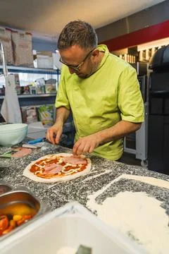 Vertical shot of a man cook adding meat and seasonings to prepare pizza Stock Photos