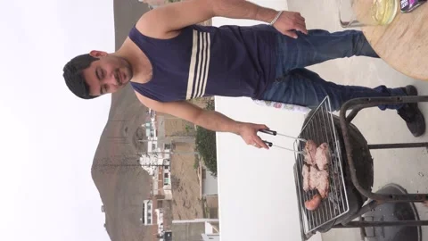 Vertical shot of a man preparing meats  on a grill on the roof of a beach house Stockbeeldmateriaal 155808257