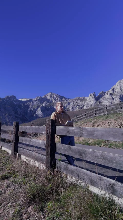 Vertical shot of man reading outdoors with rocky mountain landscape 스톡 동영상 336623093