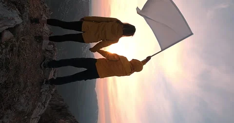 Vertical shot man waving white flag holding a woman's hand against sunset dawn Stock Footage 247406614